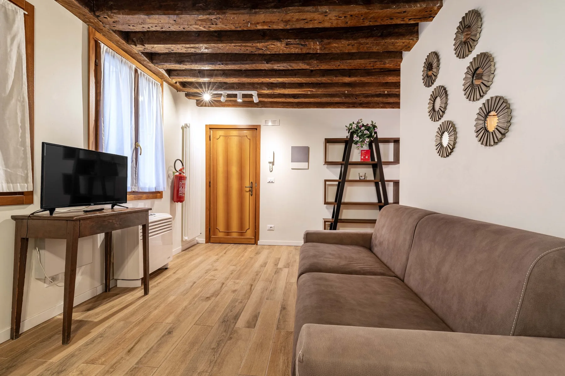 A living room with a sofa, television, and wooden ceiling beams.