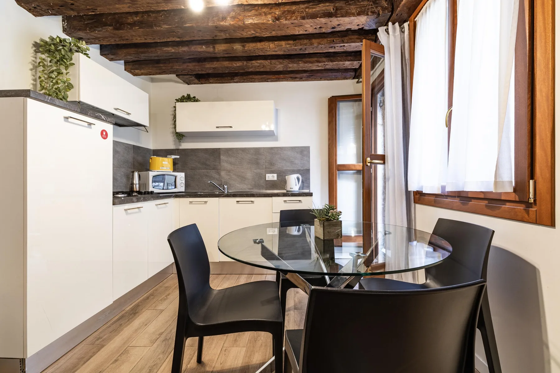 A kitchen and dining area with a glass table and dark seating.