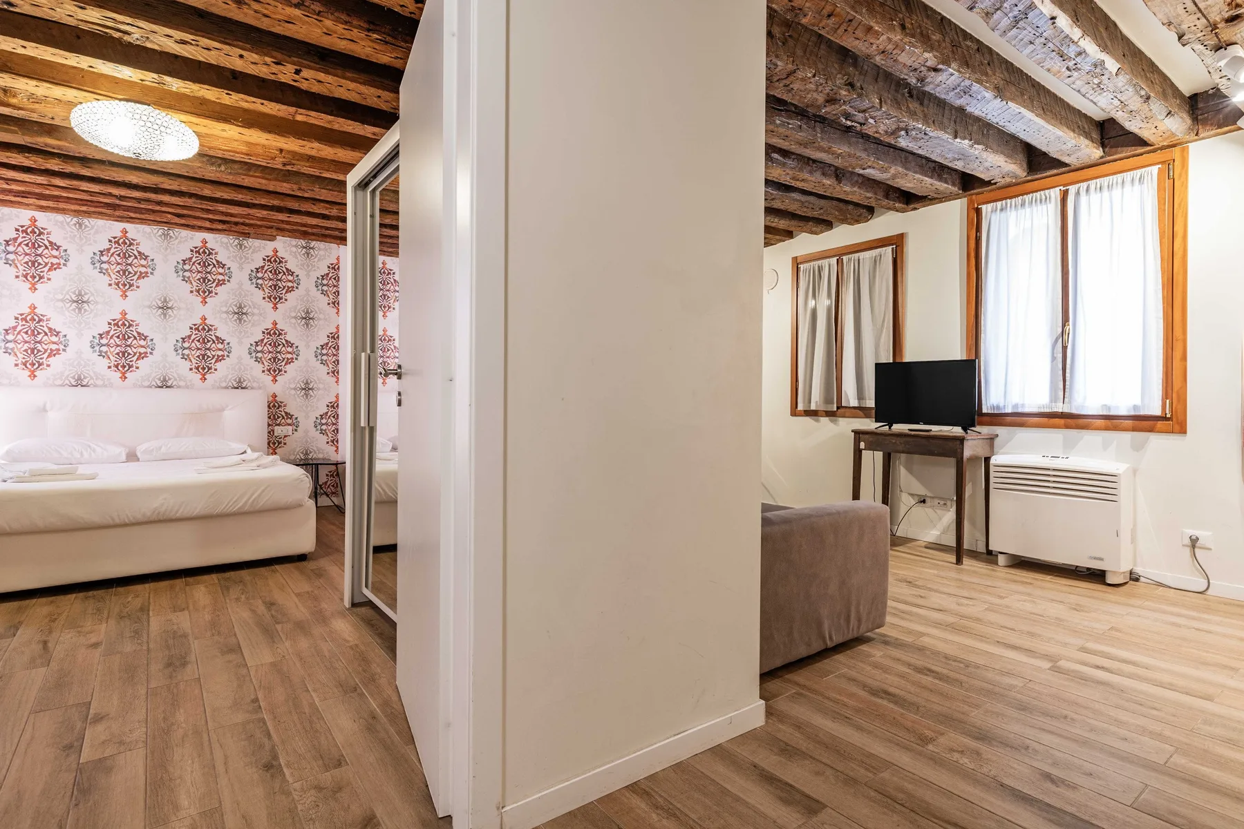 A bedroom and sitting area with a bed, television, and wood-beamed ceiling.