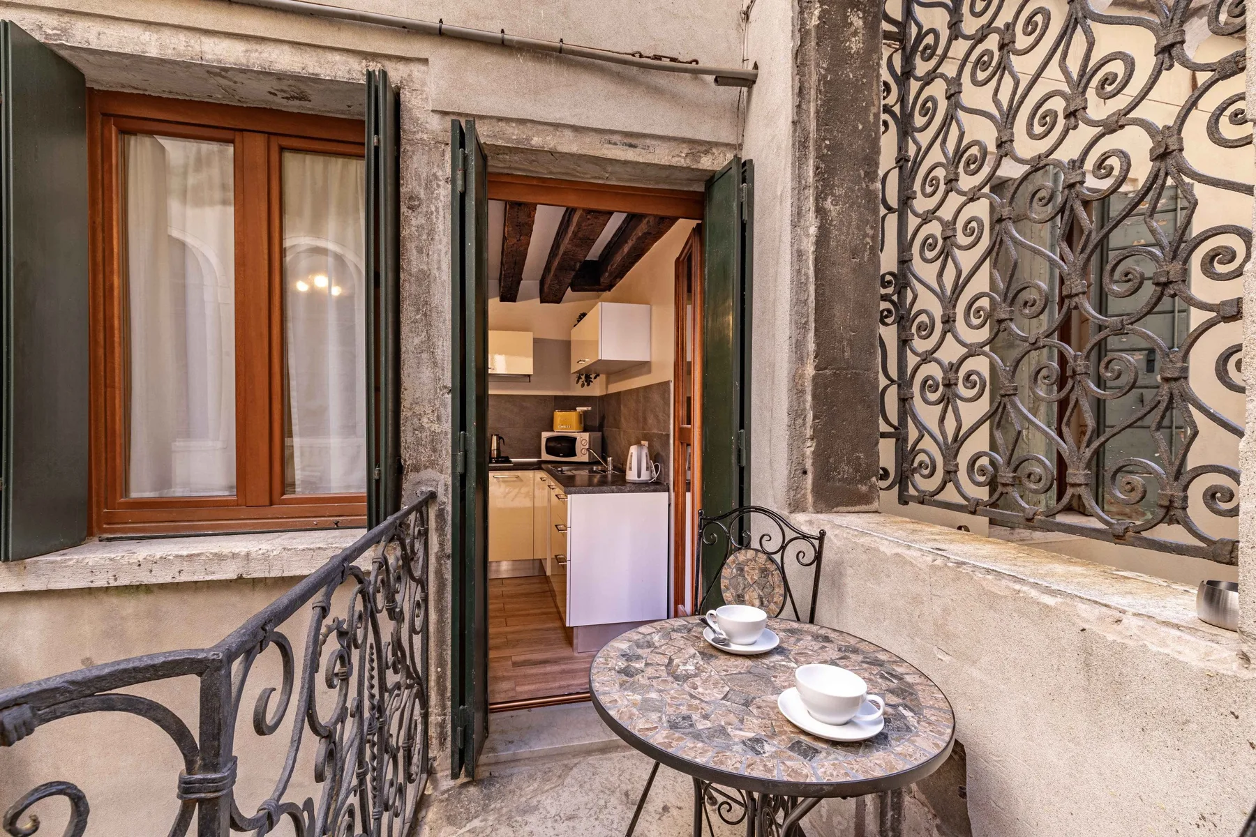 A small balcony with a round table overlooks an open kitchenette.