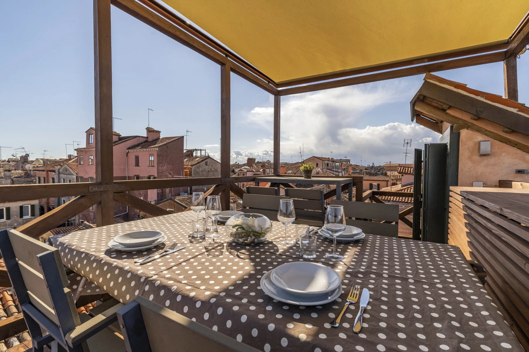 Una terraza comedor en la azotea tiene una mesa bajo un toldo.
