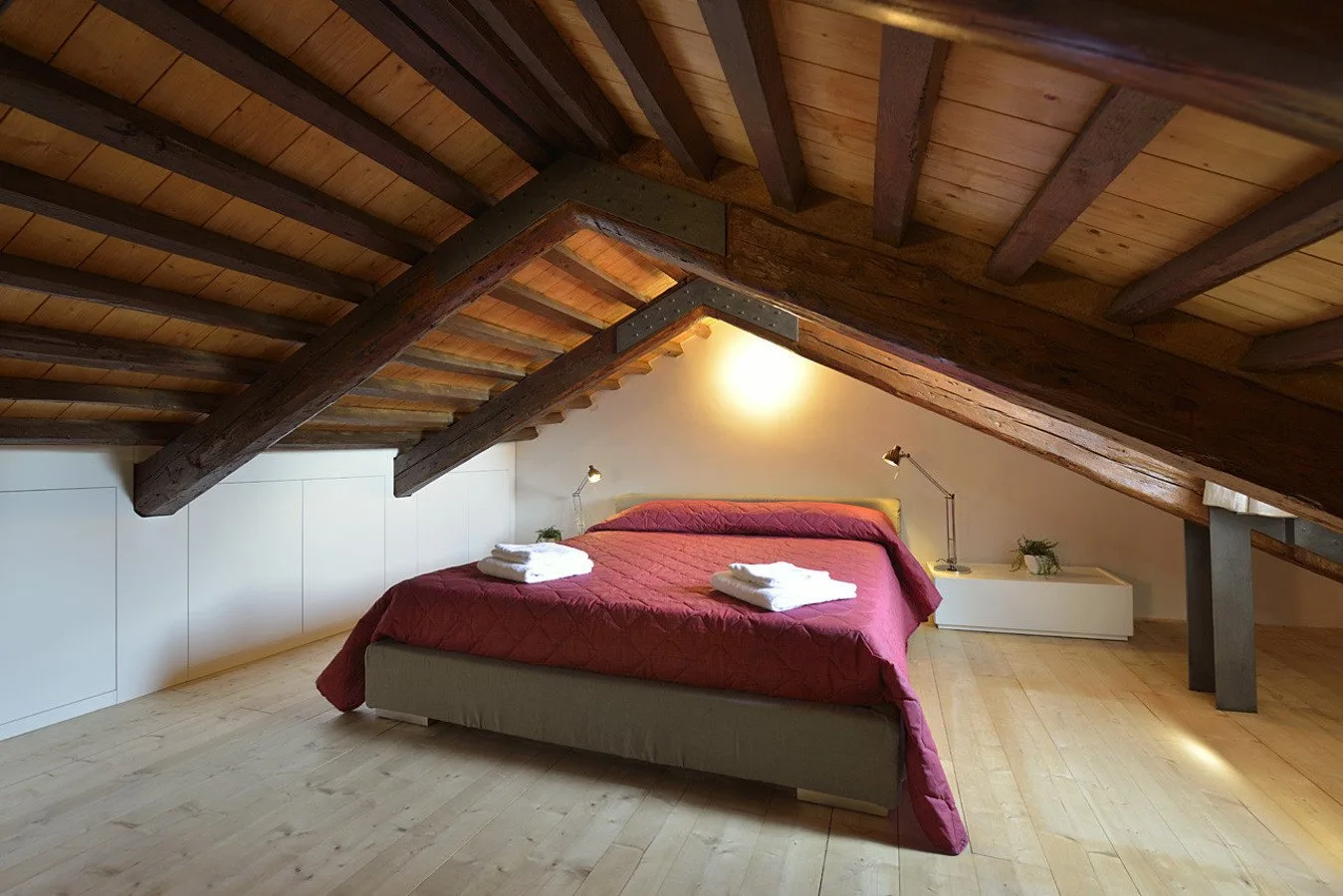 Un dormitorio con una cama bajo un techo inclinado con vigas de madera.