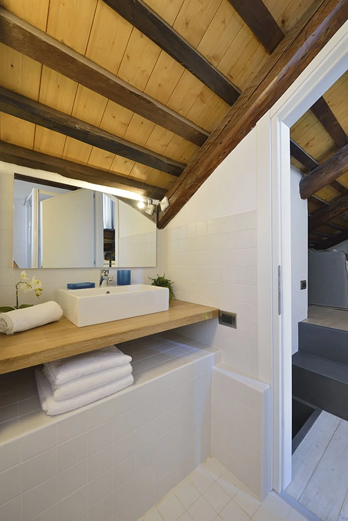 Un lavabo de baño está bajo un techo inclinado de madera, con un espejo sobre el lavabo.