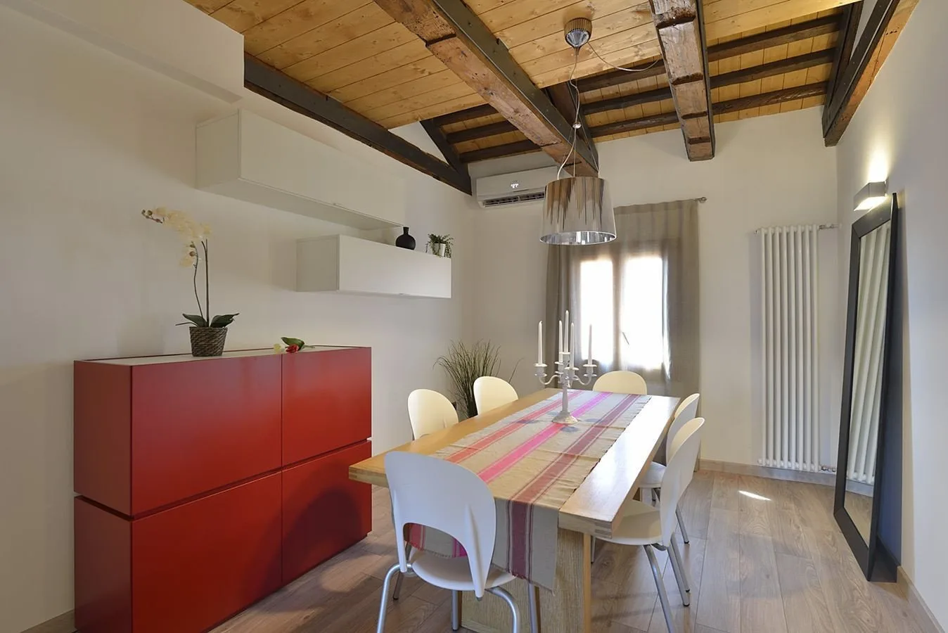 Comedor con una mesa larga y un mueble rojo bajo vigas de madera a la vista.