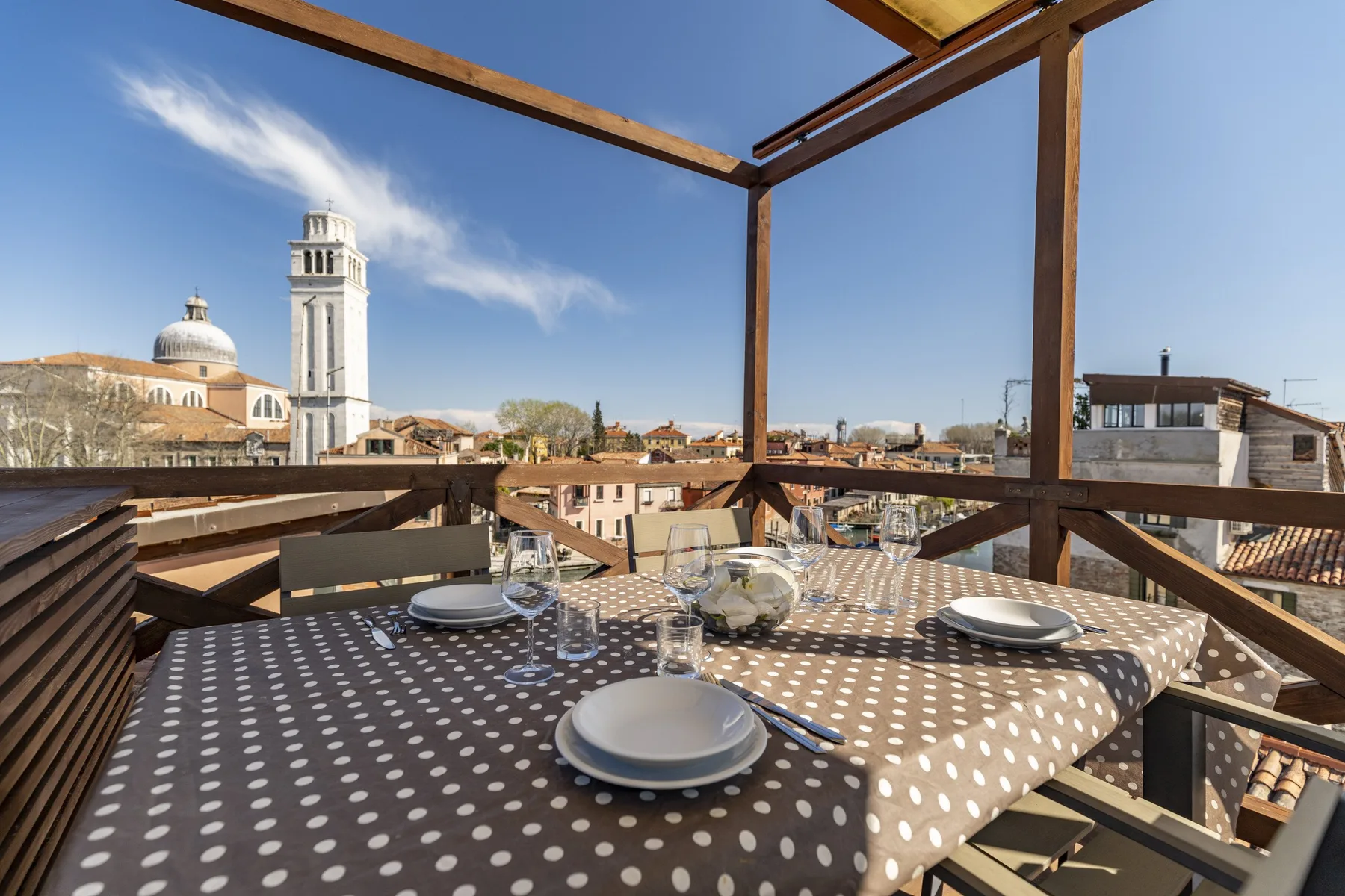 Una zona de comedor en la azotea con una mesa puesta y vistas a edificios cercanos.