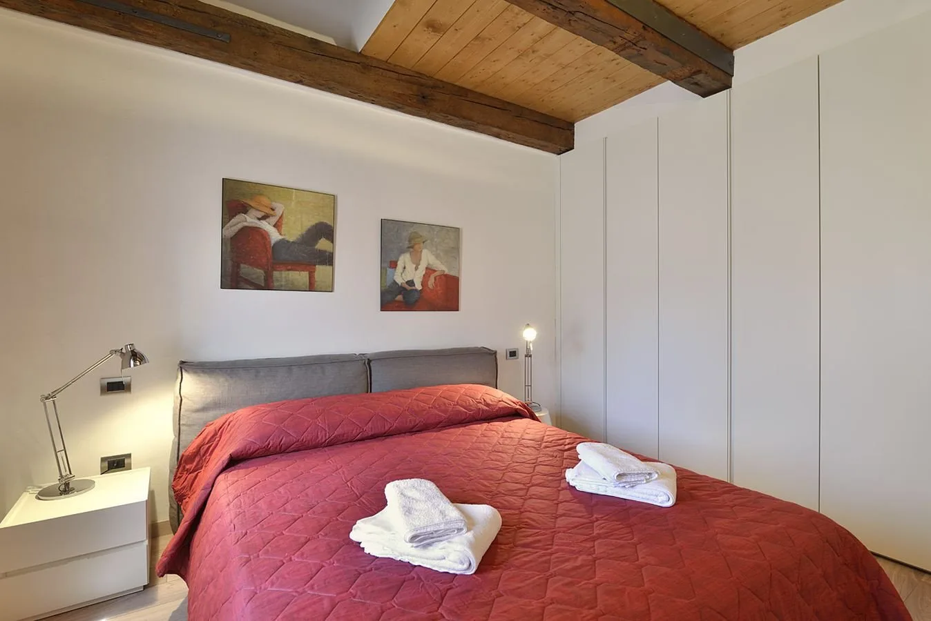 Un dormitorio con una cama cubierta por una colcha roja y dos cuadros en la pared.