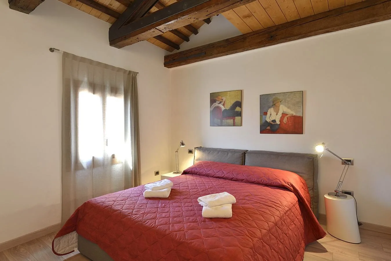 Un dormitorio con una cama grande, una colcha roja y vigas de madera a la vista.