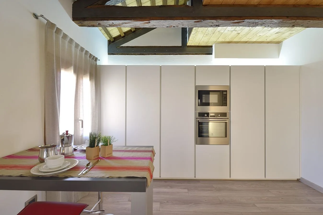 Una cocina moderna con armarios claros y hornos empotrados junto a una mesa de comedor.