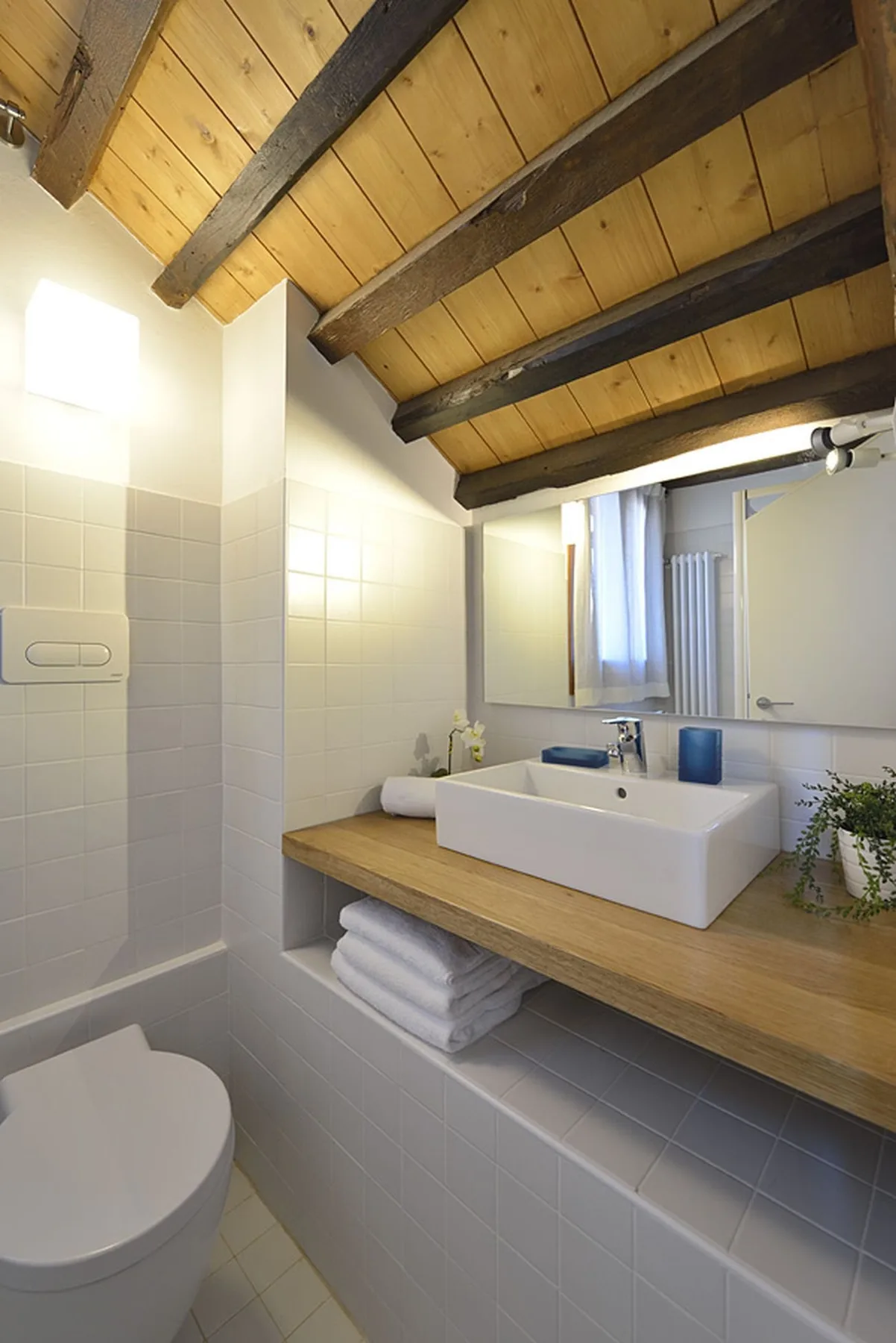 Un baño alicatado con un lavabo sobre una encimera de madera y un inodoro.