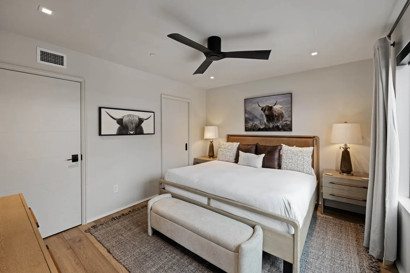 A bedroom with a bed, upholstered bench, and framed animal artwork.