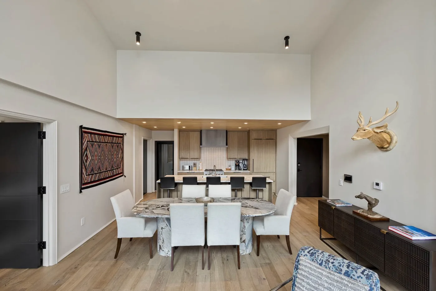 A dining area with a long table and chairs sits in front of an open kitchen.