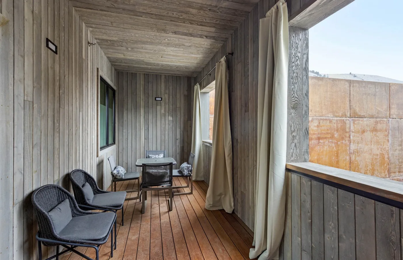 A narrow wood-paneled room with seating and curtains beside an open window.