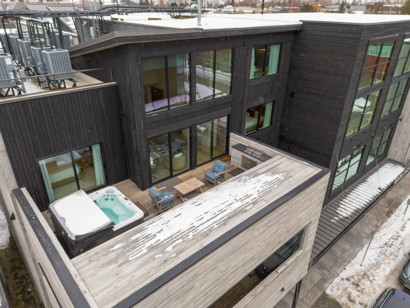 A modern building surrounds an outdoor terrace with seating and a hot tub.