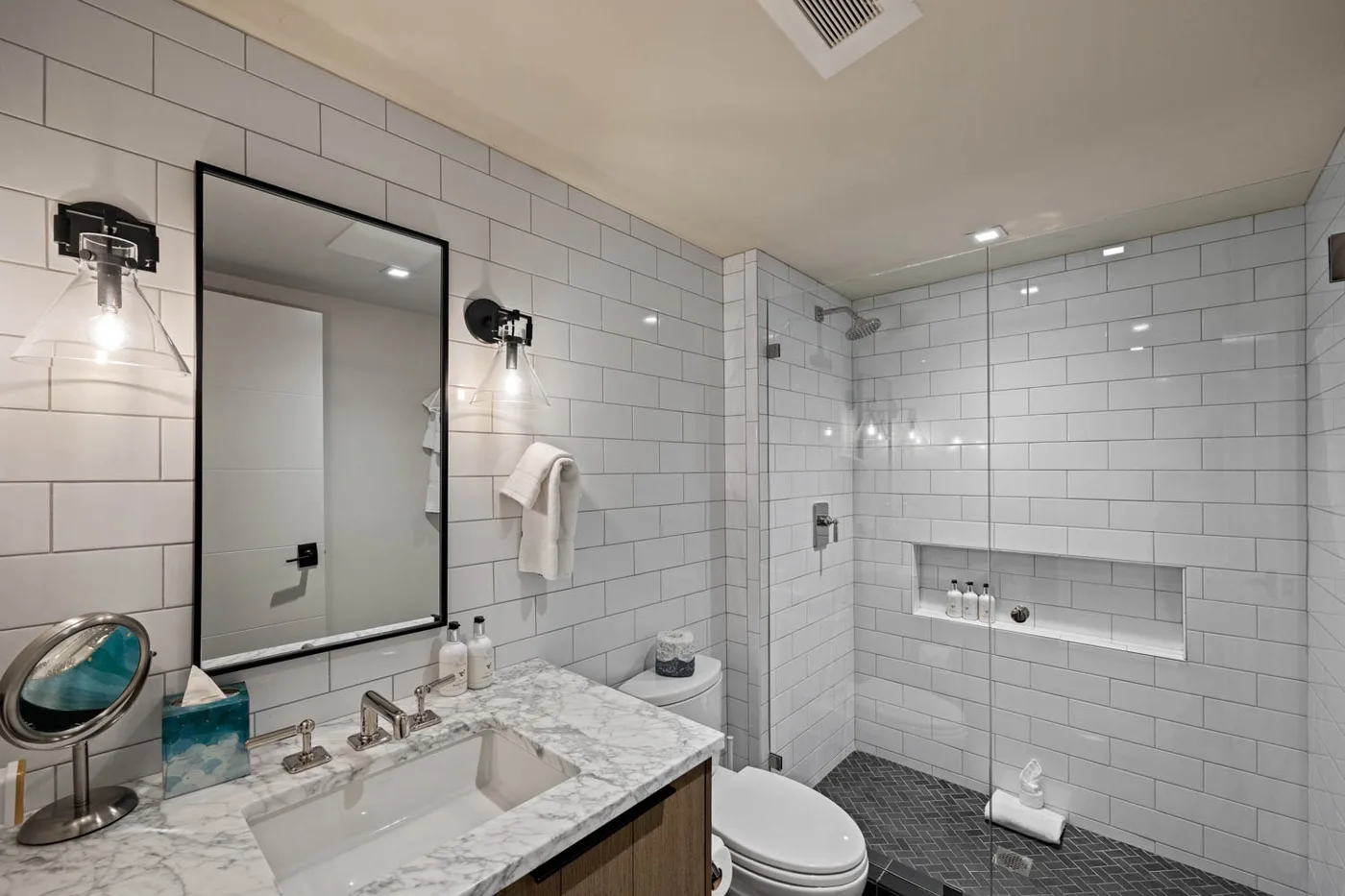 A tiled bathroom with a marble vanity, mirror, and shower.