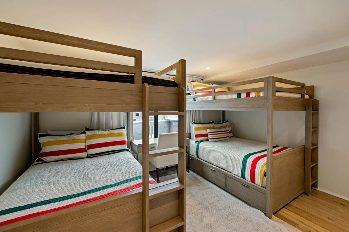 A bedroom with two wooden bunk beds and colorful striped bedding.