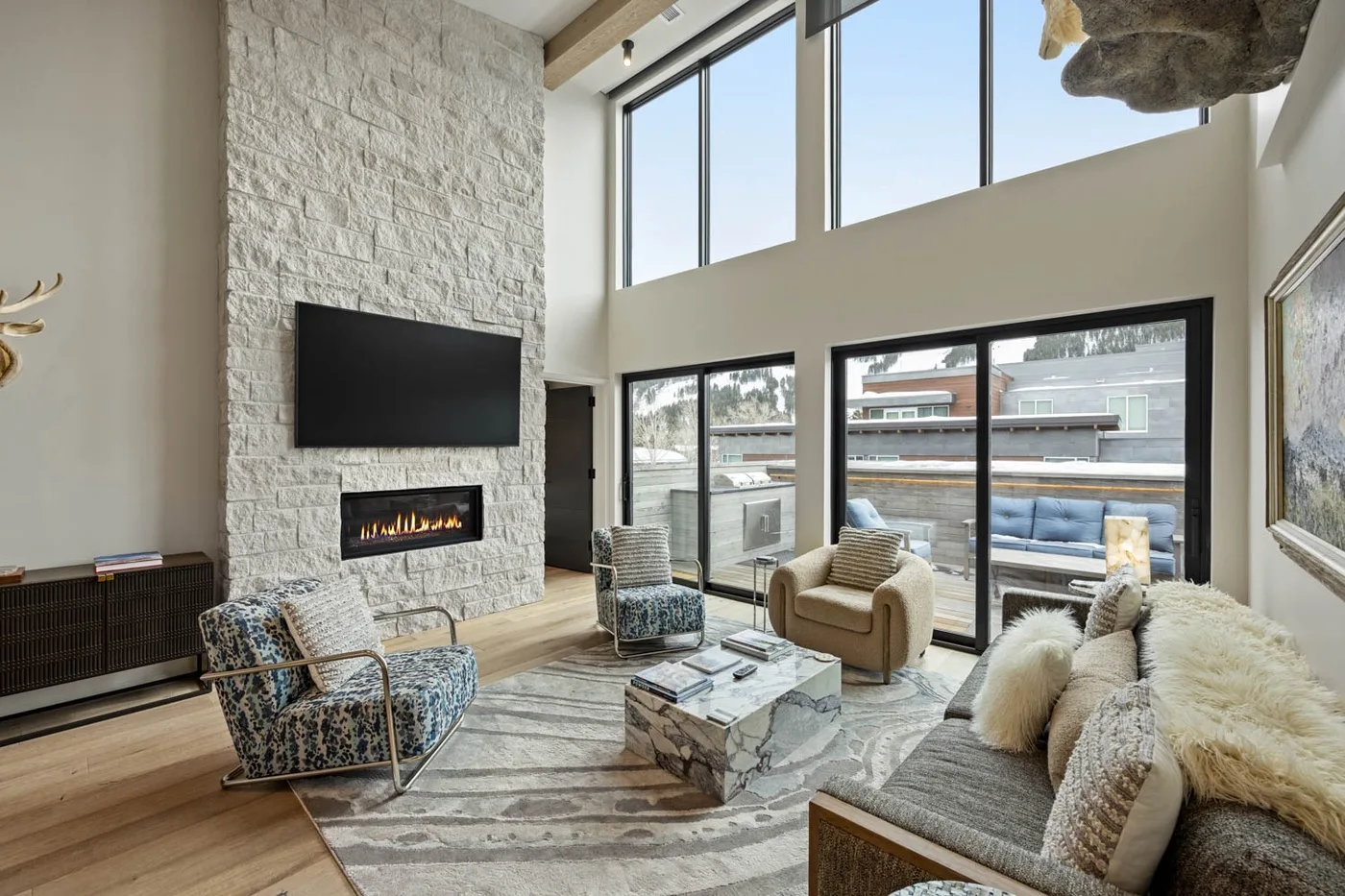 A bright living room with seating, a stone-textured wall, and large windows.