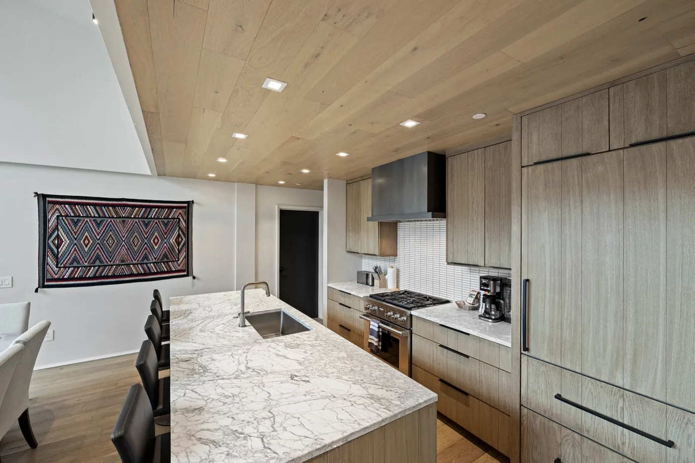 Kitchen with a large island, built-in appliances, and light wood cabinetry.