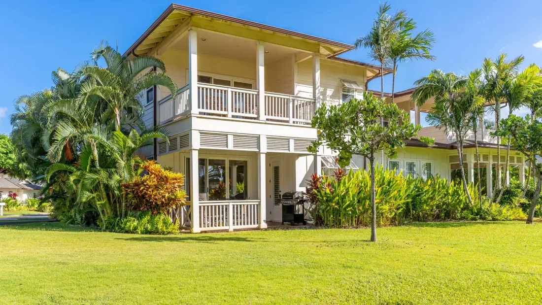 A two-story house with balconies stands behind a broad green lawn.