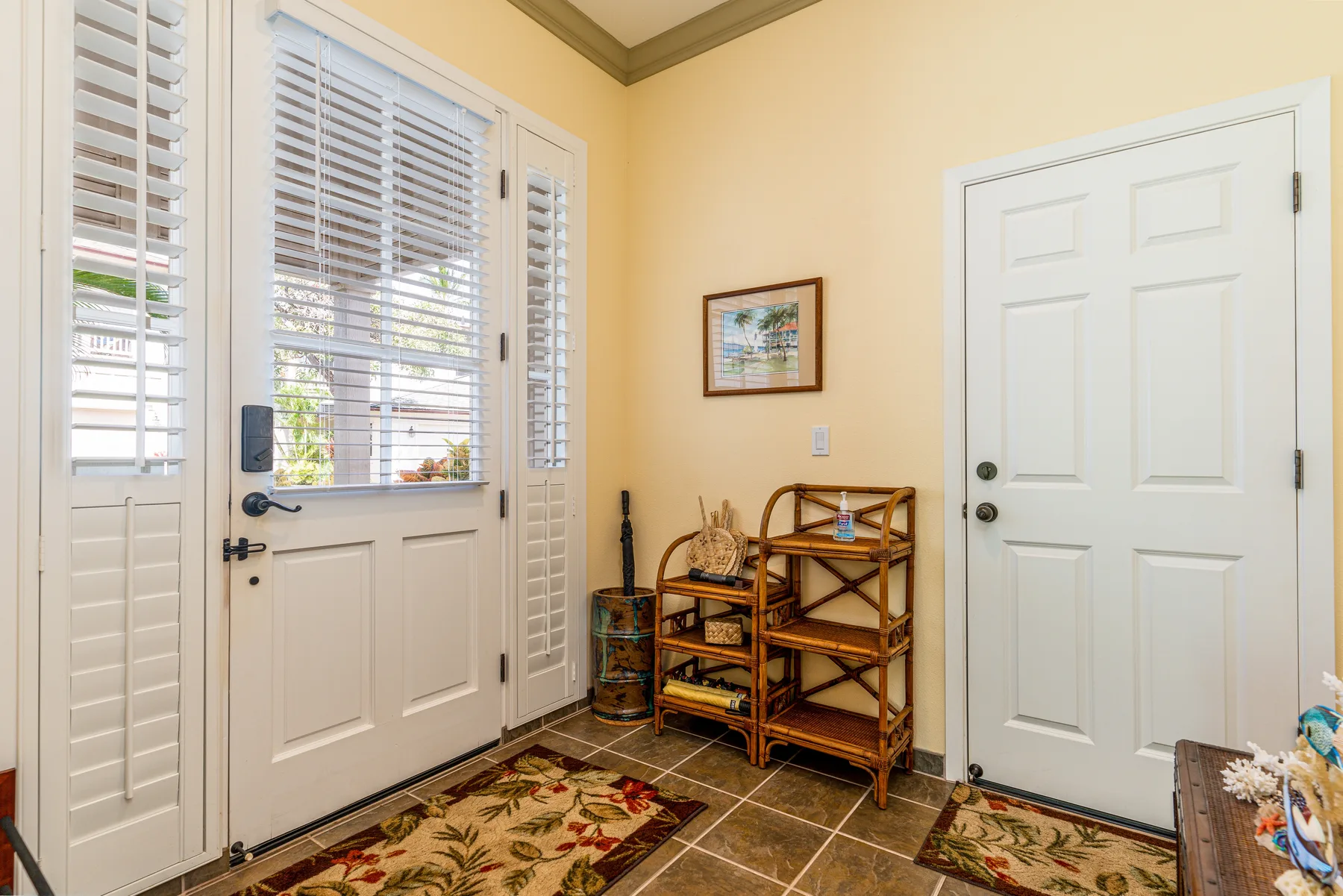 A bright entryway with shuttered glass doors, a small shelving unit, and a patterned rug.