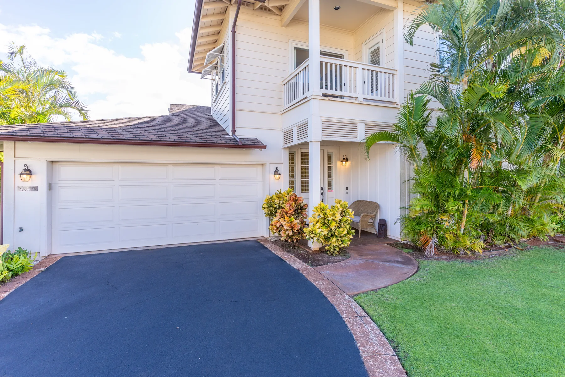 A house exterior with a wide driveway, garage door, and tropical landscaping.