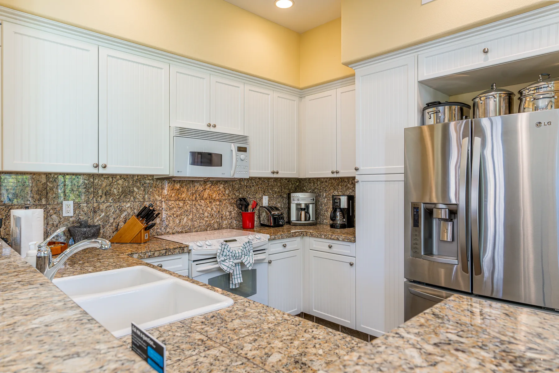 A bright kitchen with white cabinets, stone counters, and stainless steel appliances.