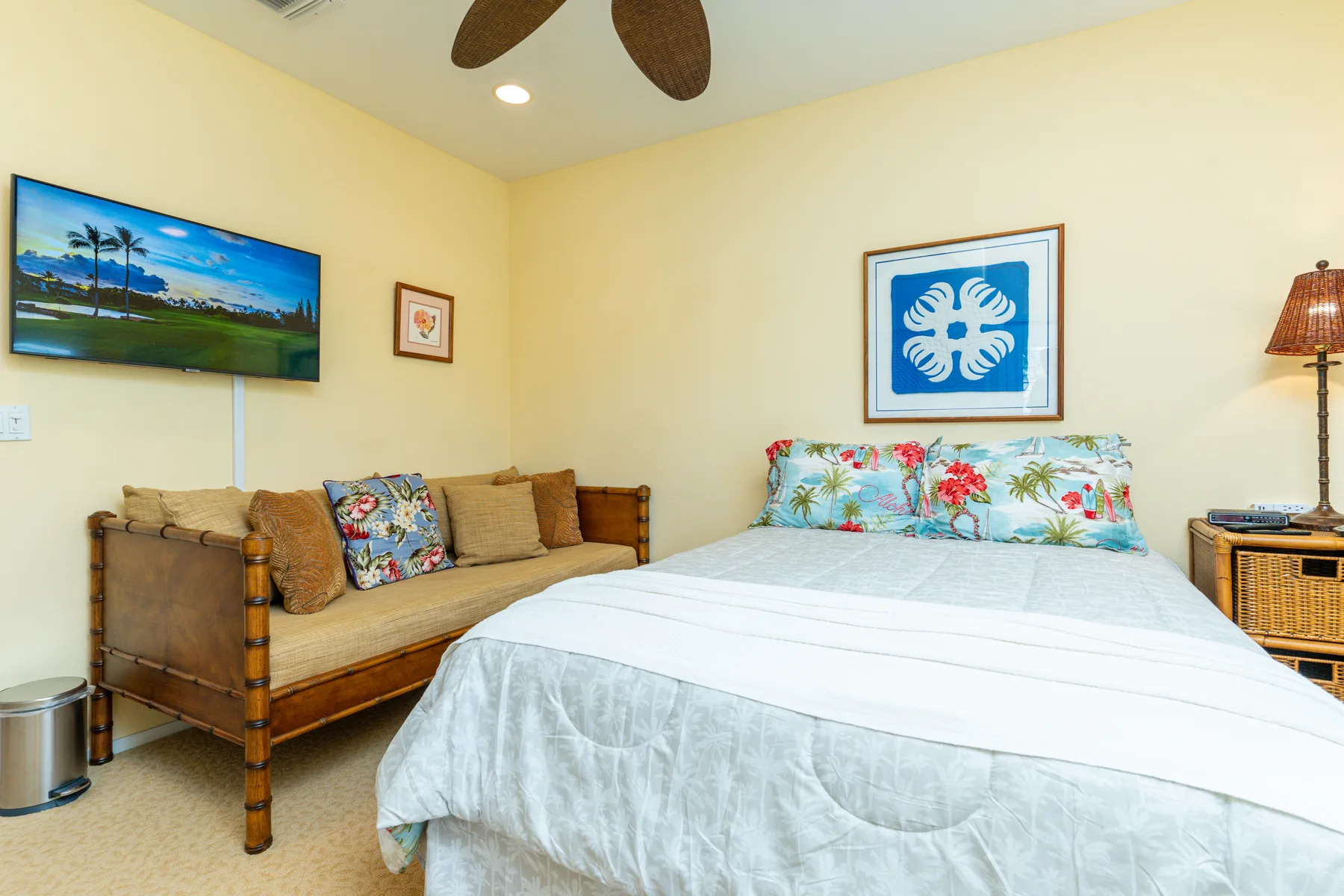 A bedroom with a bed and a wooden seating area beneath a wall-mounted television.
