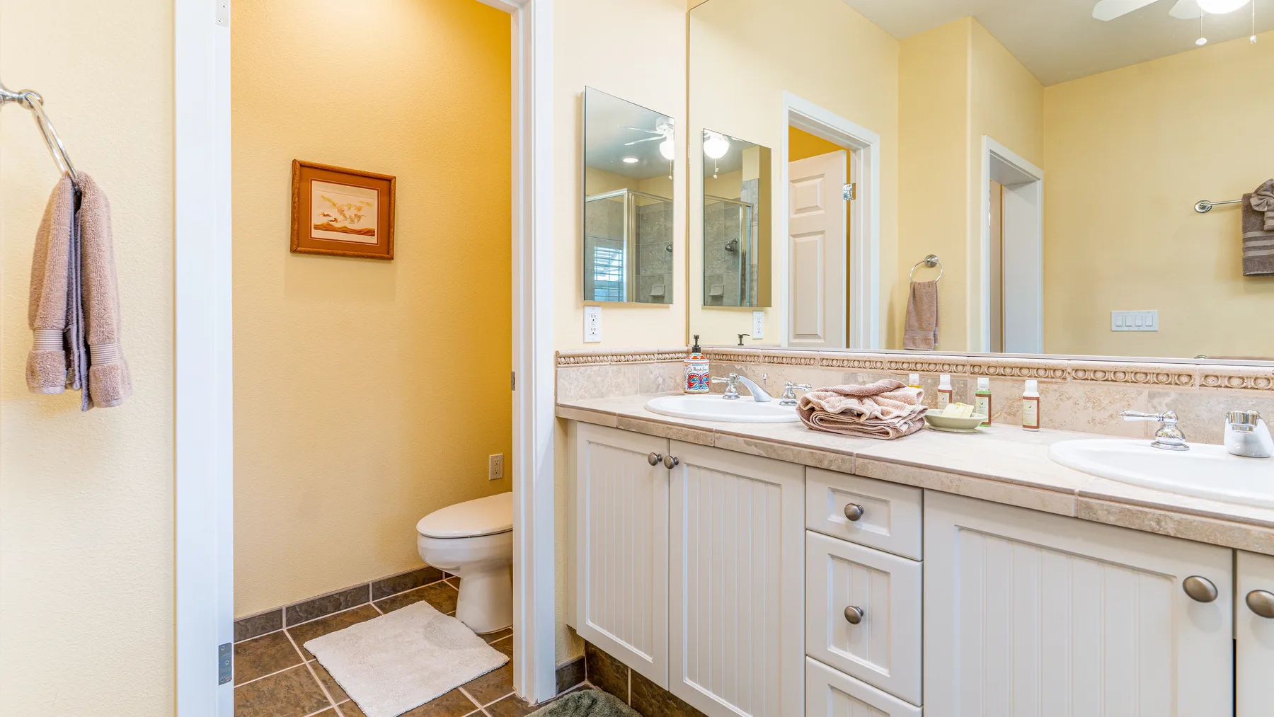 A bright bathroom vanity with a long counter and a toilet in an adjoining alcove.