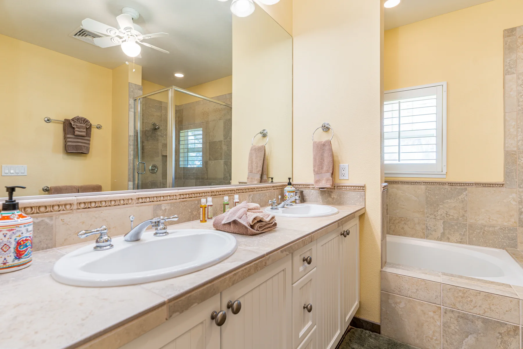 A bathroom with a double vanity, large mirror, and bathtub.