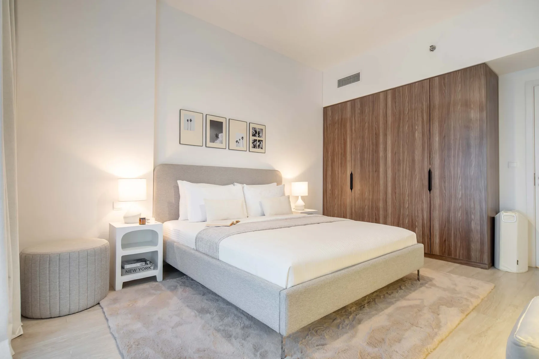 Un dormitorio con una cama tendida, mesitas de noche y un armario grande de madera.