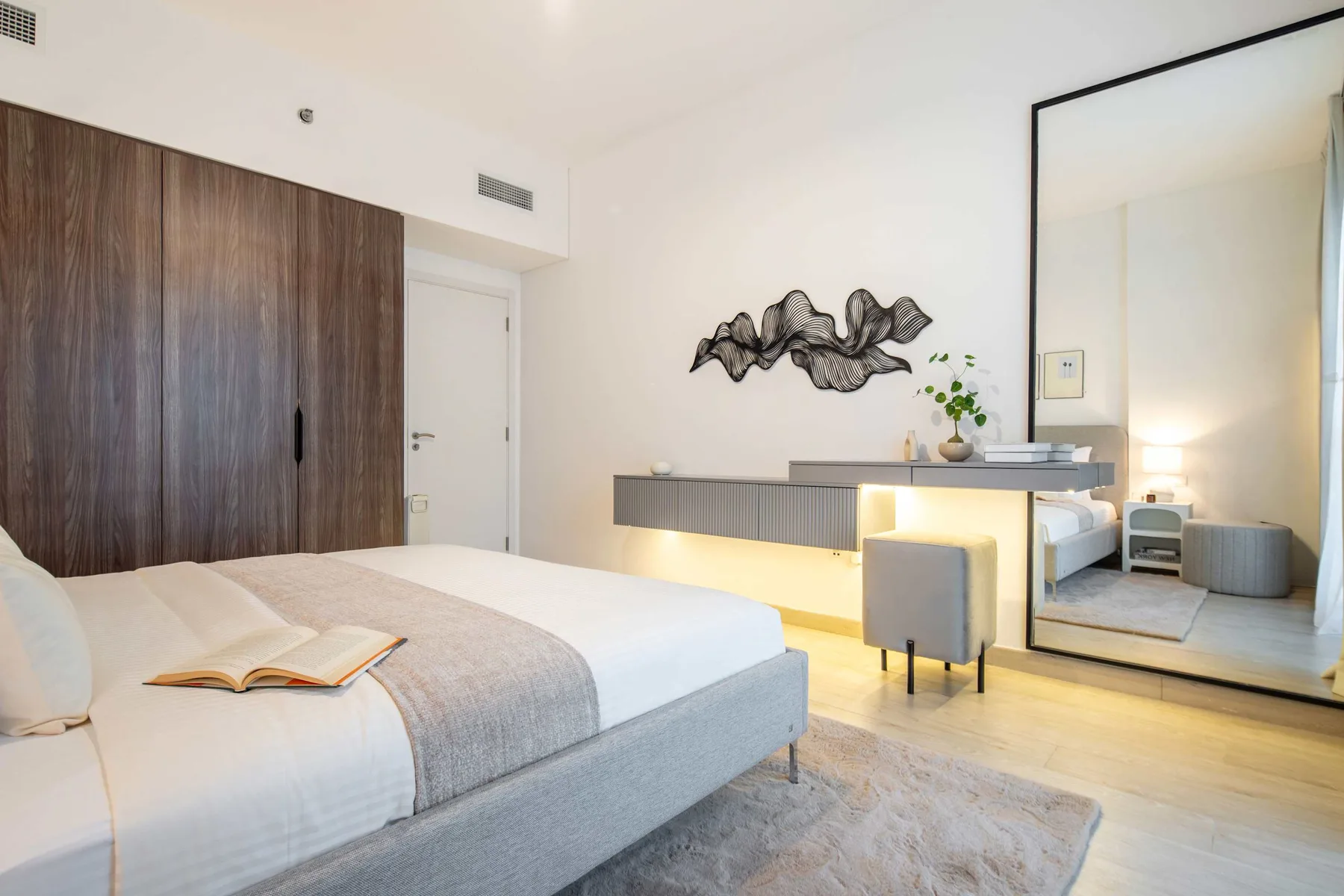 Un dormitorio moderno con una cama, un escritorio de pared y un espejo grande.