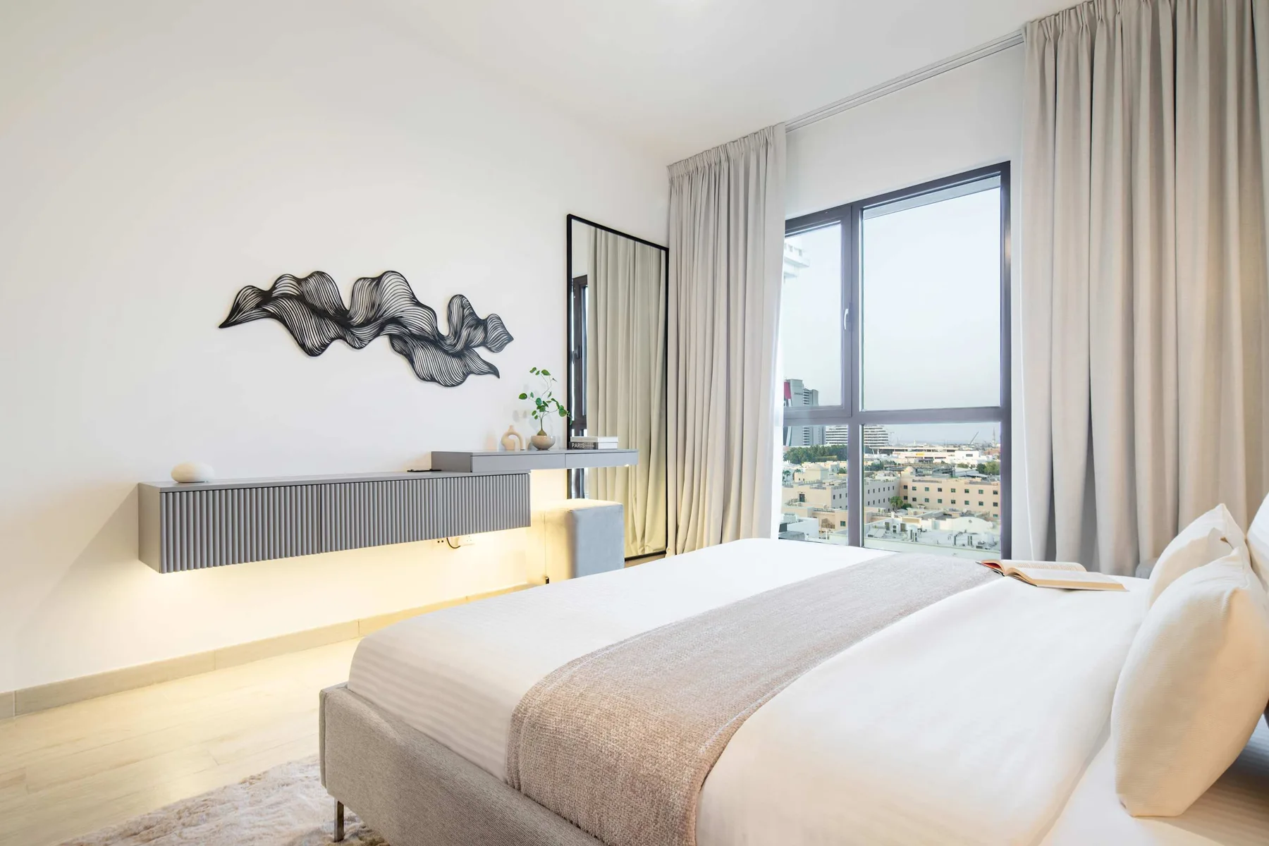 Un dormitorio luminoso con una cama, arte mural y una gran ventana enmarcada por cortinas.
