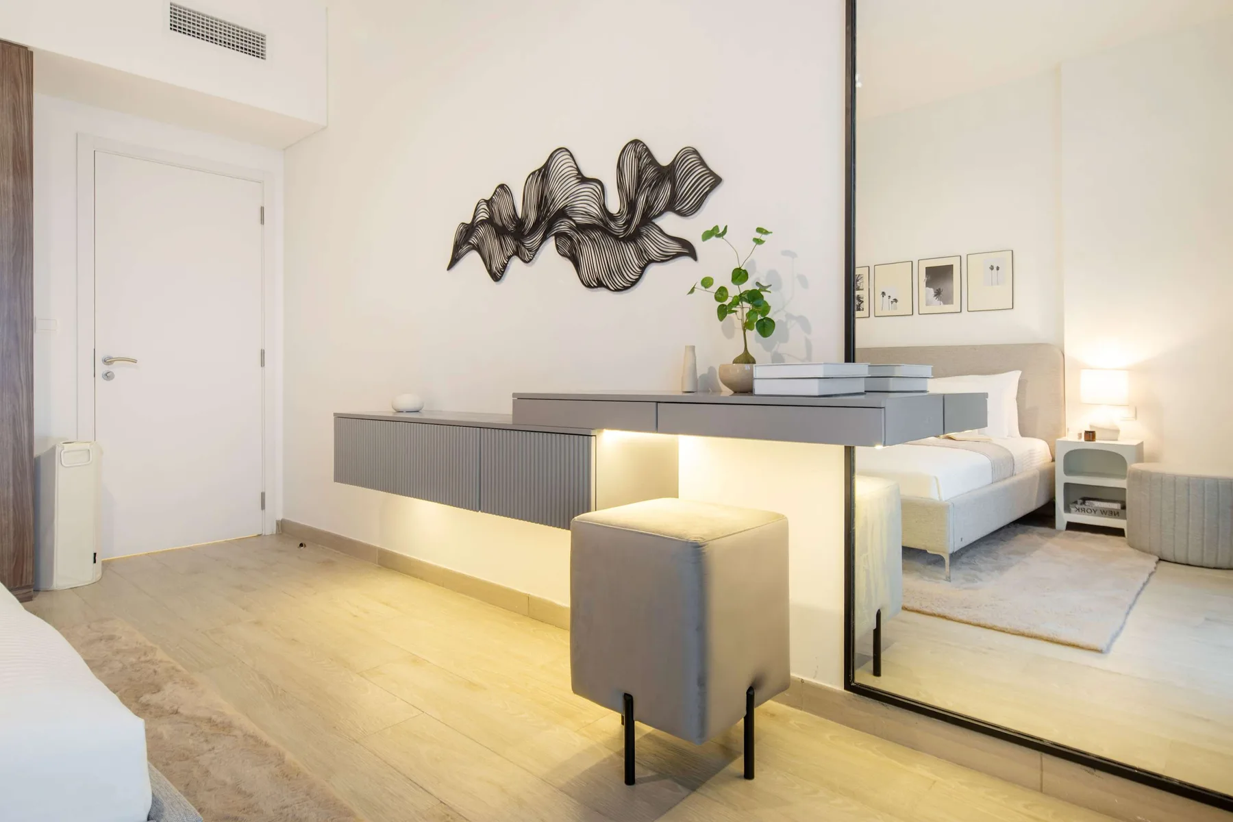 Un dormitorio luminoso con una cama, un escritorio flotante y arte mural escultórico.