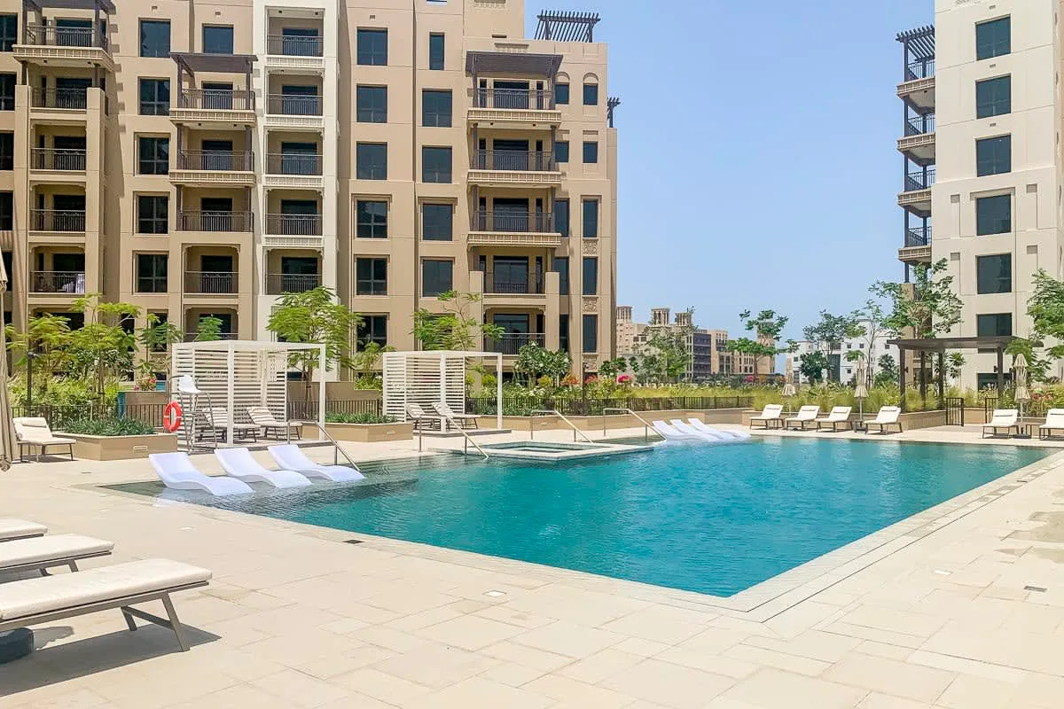 Una piscina al aire libre está rodeada de edificios de apartamentos y asientos.