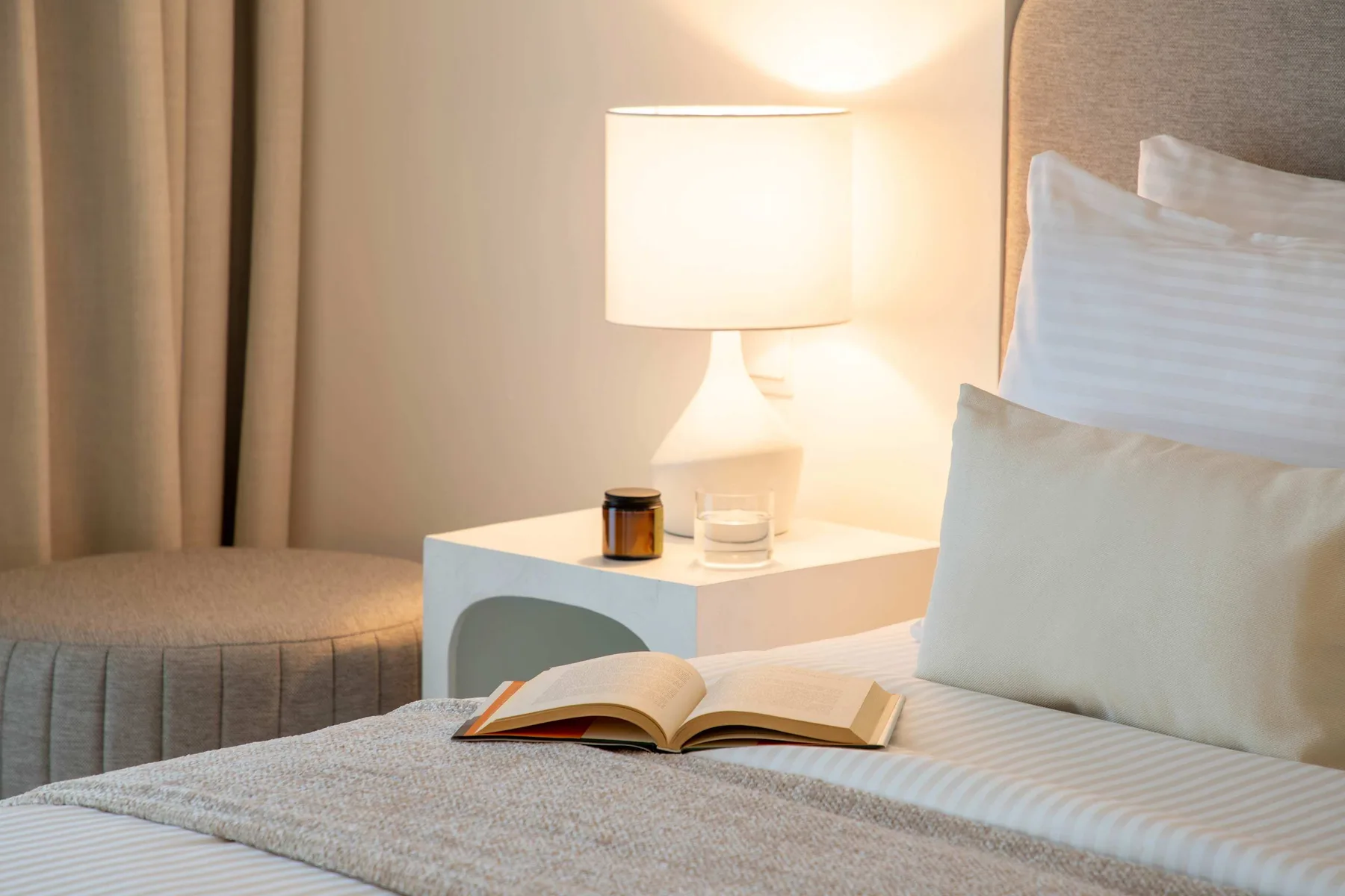 Dormitorio con luz cálida, un libro abierto sobre la cama y una lámpara.