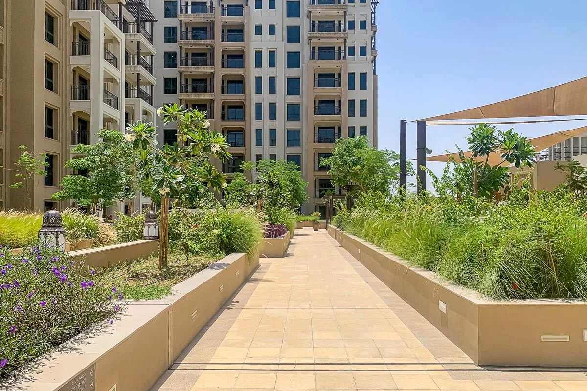 Un sendero ajardinado atraviesa un patio entre parterres y edificios residenciales.