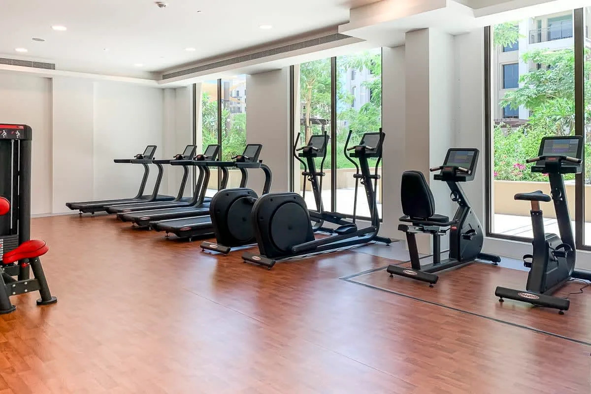 Una sala de ejercicios luminosa con cintas de correr y máquinas junto a grandes ventanales.