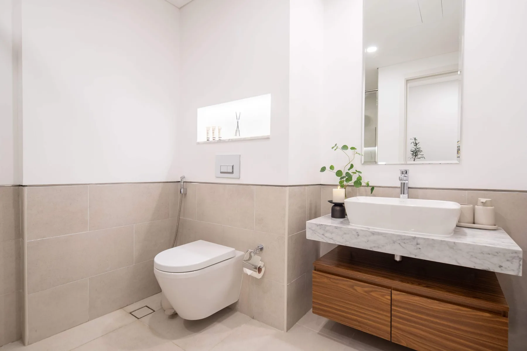 Un baño luminoso con un inodoro suspendido y un tocador con lavabo sobre encimera.