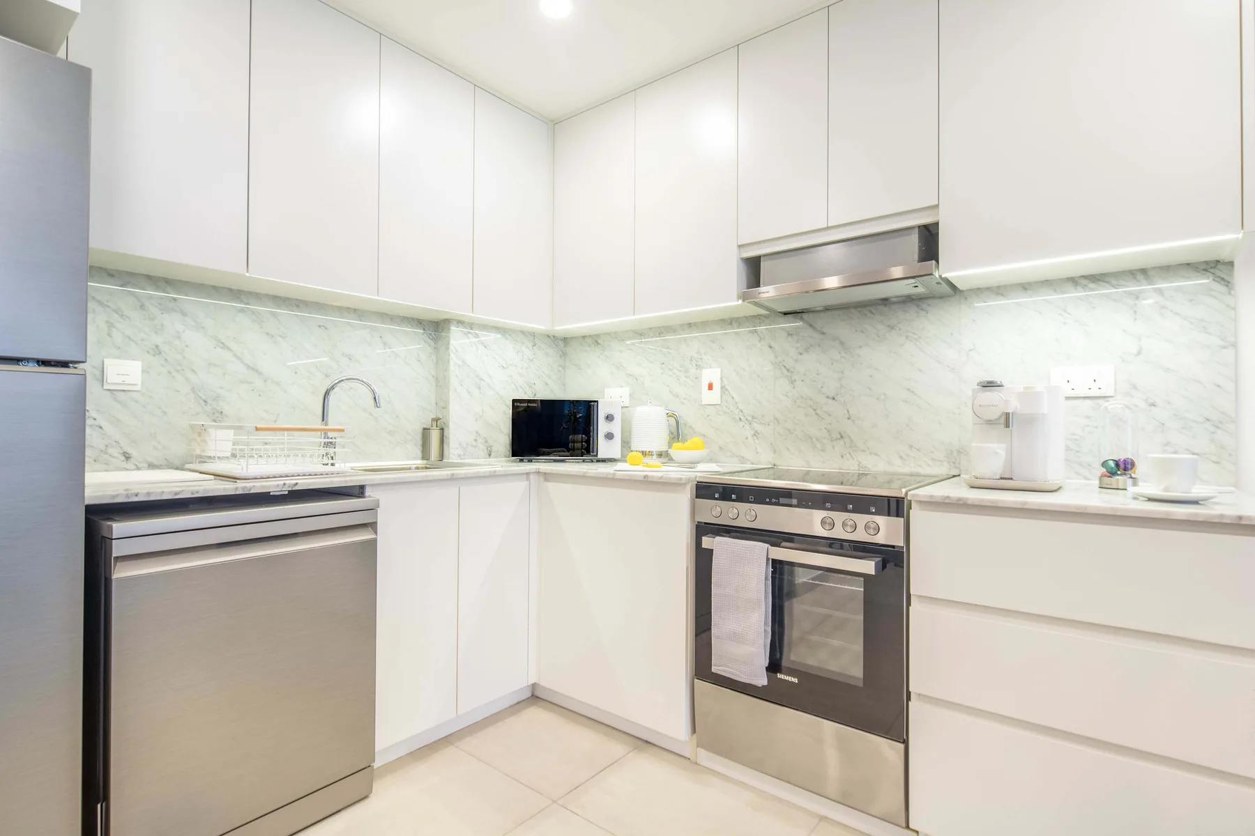 Una cocina moderna y luminosa con gabinetes blancos y electrodomésticos de acero inoxidable.