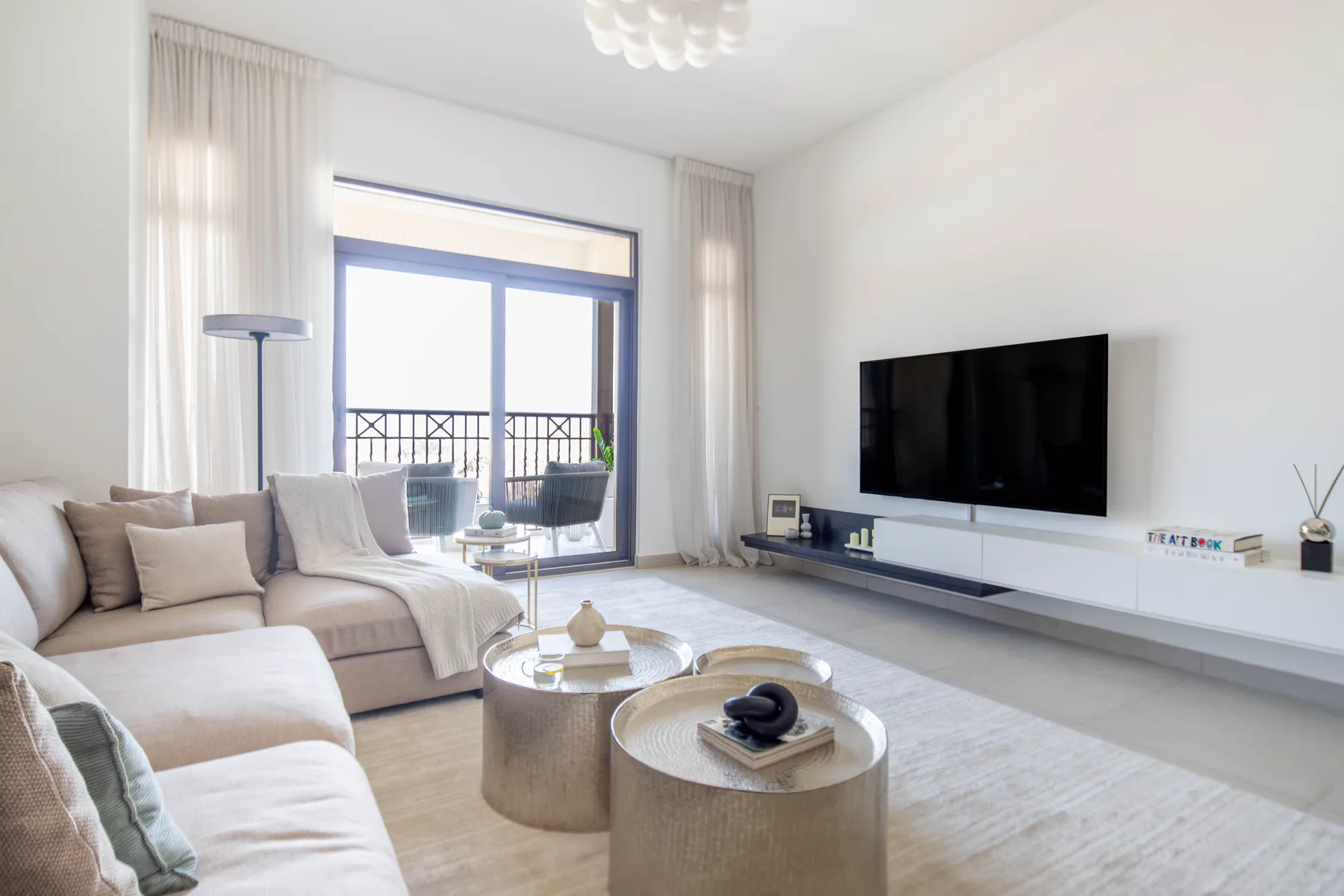 Sala de estar luminosa con asientos, mesas bajas y un televisor.