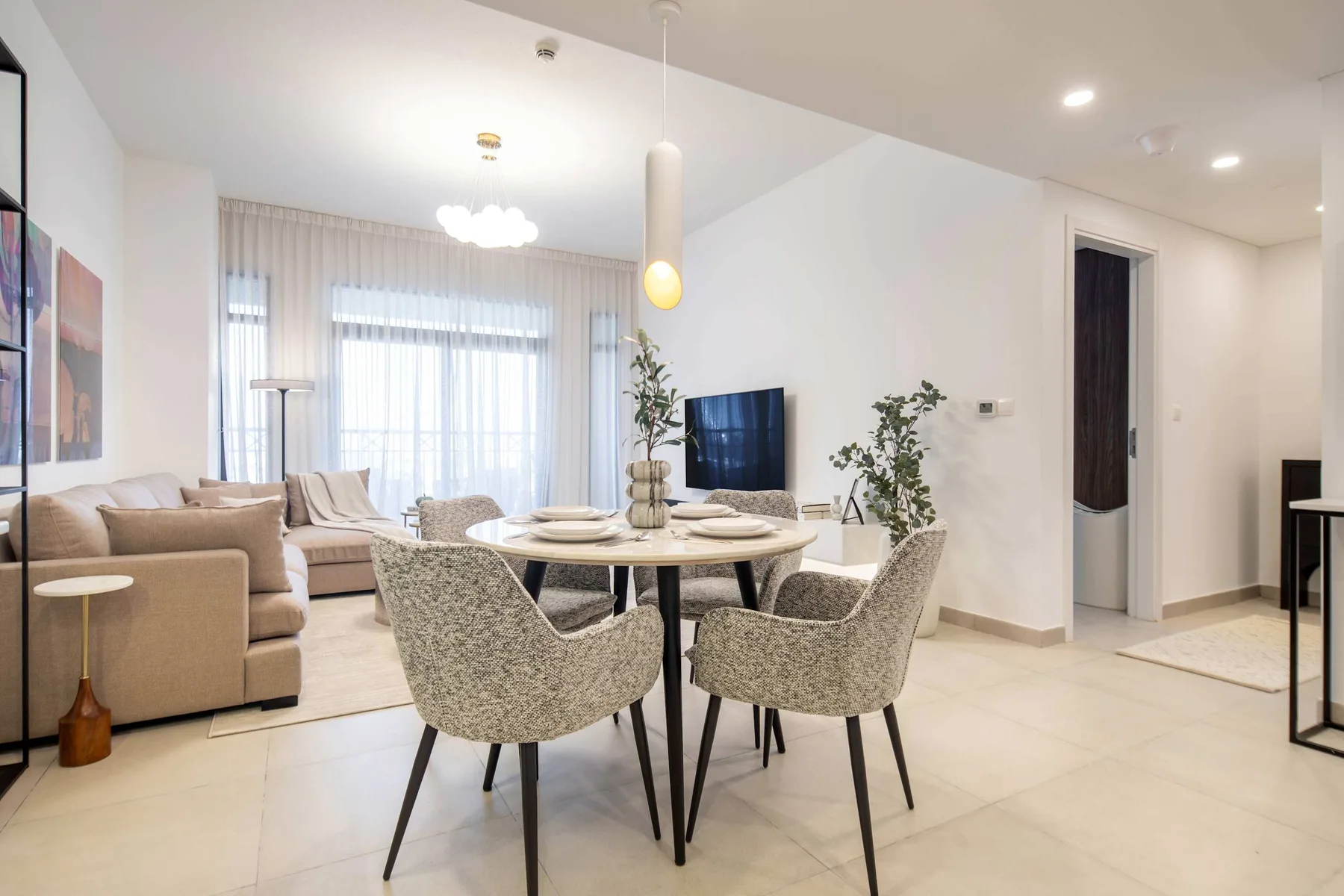 Una luminosa sala de estar y comedor con asientos alrededor de una mesa y un televisor.