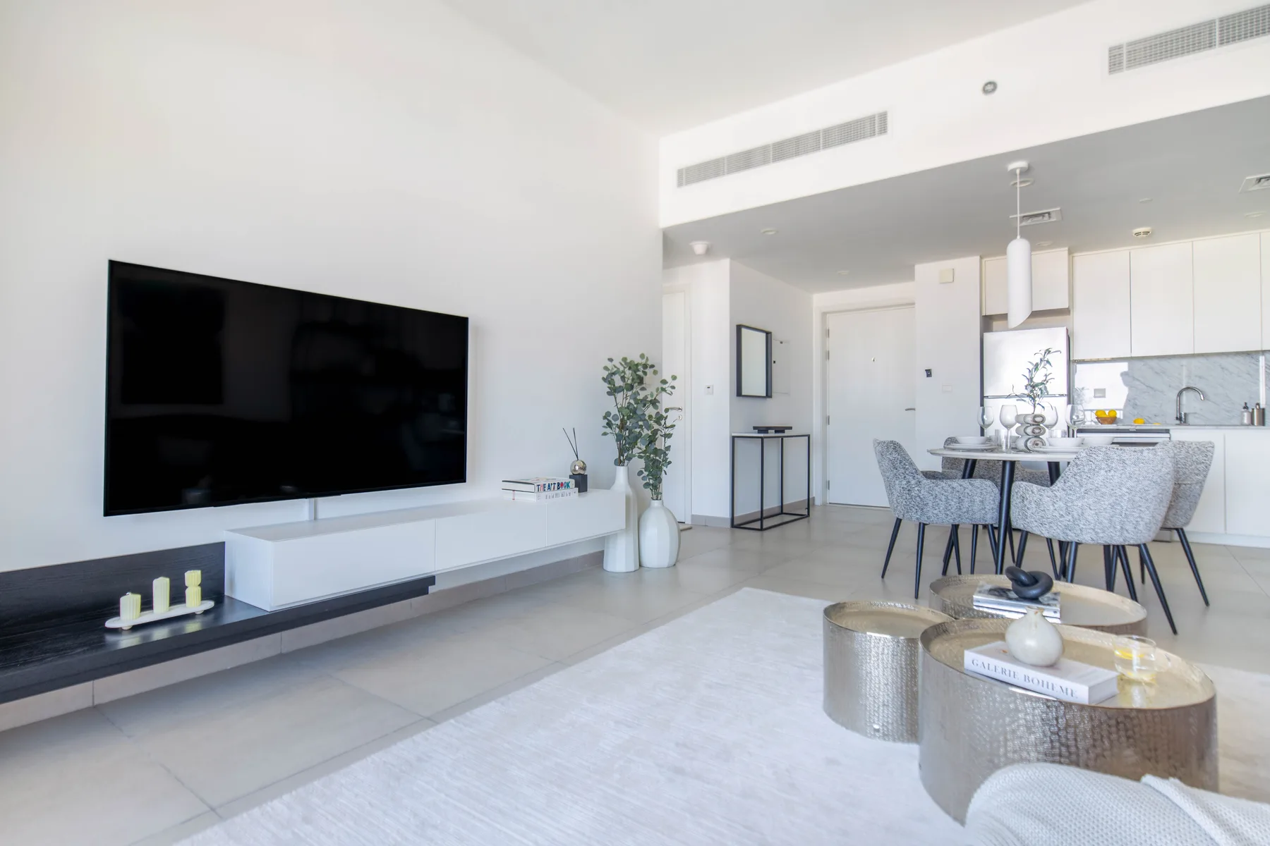 Una luminosa sala de estar y comedor de planta abierta, con televisor en la pared y mesa de comedor.