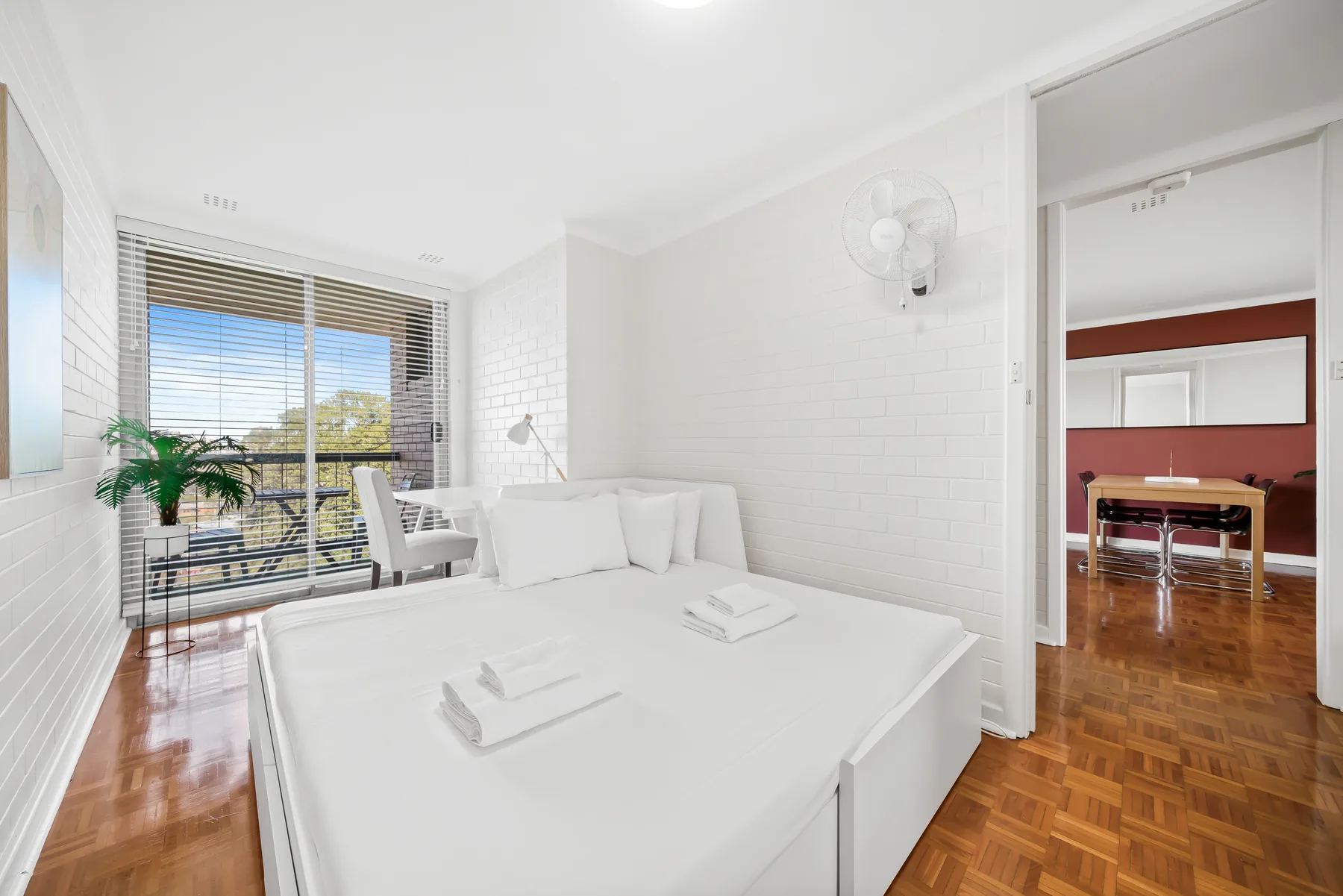 A bright bedroom with white bedding and a window overlooking greenery.