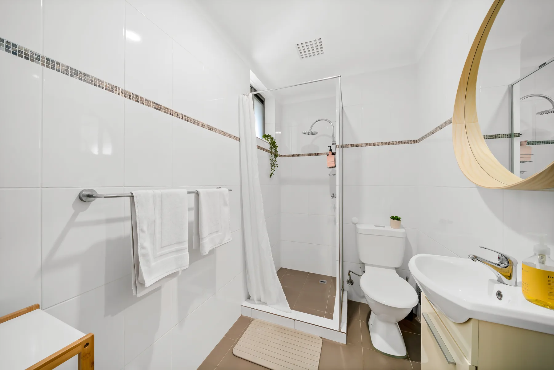 A bright tiled bathroom with a glass shower, toilet, and sink.