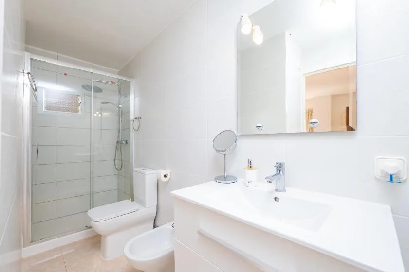 A bright bathroom with a glass shower, toilet, and sink.