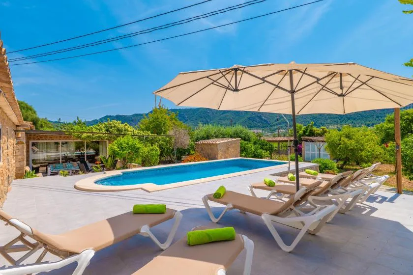 An outdoor swimming pool with loungers and a large umbrella on the surrounding patio.