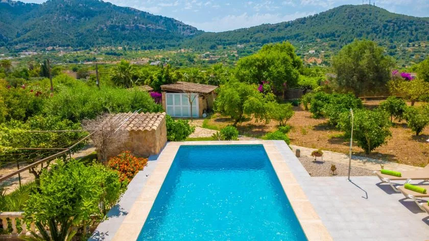 An outdoor swimming pool sits among garden greenery with hills in the background.