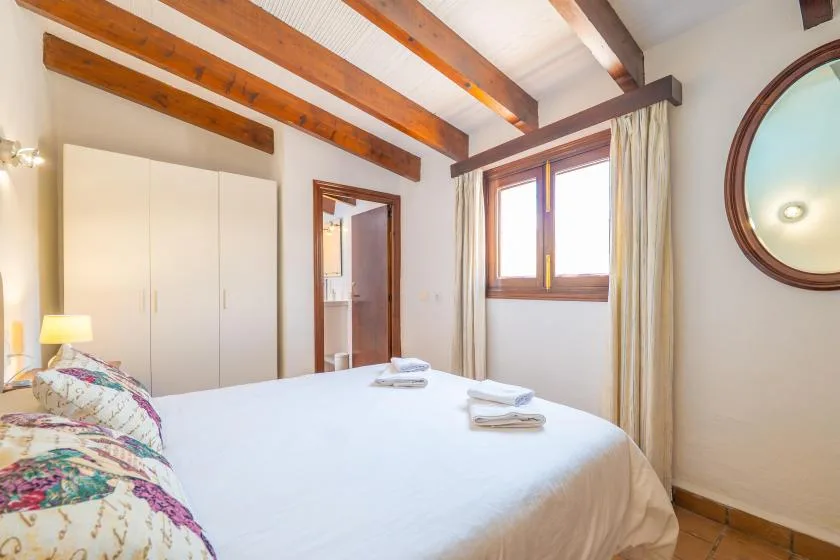 A bright bedroom with a bed, a window, and exposed ceiling beams.