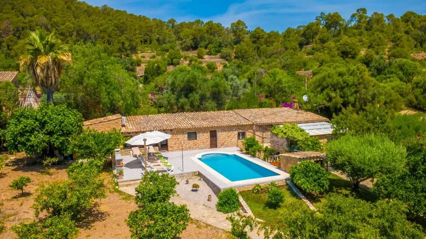 A swimming pool and patio sit beside a low building amid green wooded hills.