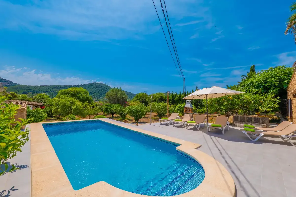 An outdoor swimming pool sits beside a sunlit patio with lounge seating.