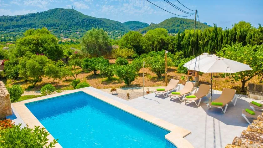 An outdoor swimming pool with lounge seating overlooks green hills and trees.